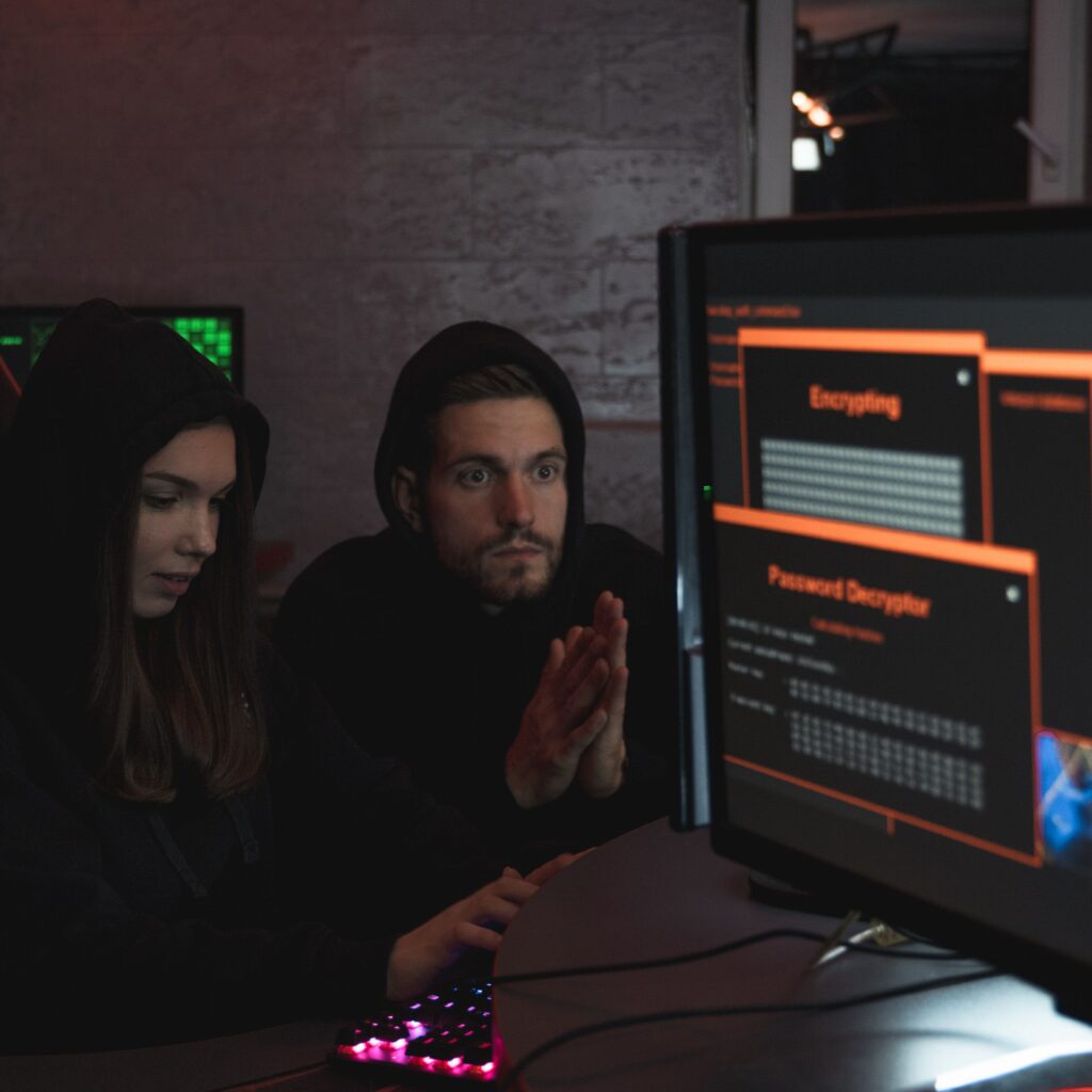 Cybersecurity experts in hoodies analyzing encrypted data on computer screens in an indoor setting.