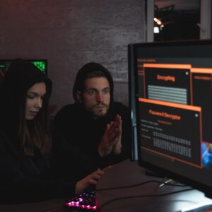 Cybersecurity experts in hoodies analyzing encrypted data on computer screens in an indoor setting.